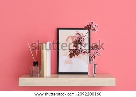 Book shelf with blossoming branches and picture hanging on color wall