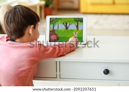 Little boy watching cartoons on tablet computer at table in living room