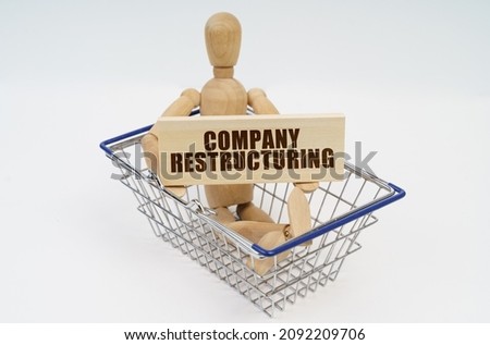 Business and finance concept. A wooden man sits in a shopping basket, holding a sign in his hands - Company Restructuring