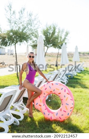 A beautiful woman holds an inflatable circle in her hands, standing on the green grass. Attractive model with perfect body. Vacation concept, the girl goes to swim in the sea