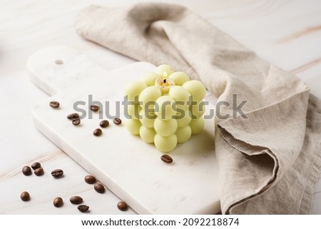 A pale green square bubble candle on a marble kitchen table among coffee beans and sweet dessert - chocolate mouse