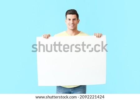 Young man with blank poster on color background