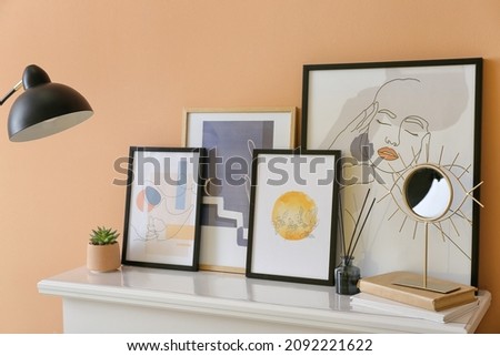 Stylish pictures and mirror on mantelpiece near color wall