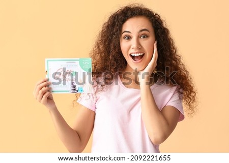 Surprised young woman with gift certificate for massage on color background