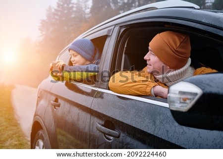 Happy father and son Sitting together in a new car on a journey. Family are resting on the side of the road on a road trip. Child takes pictures on smartphone. Happy family travels.