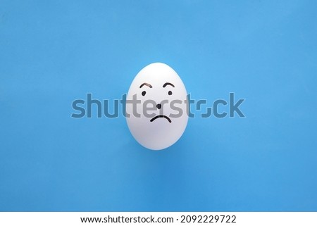 
One emotion painted egg depicting a startled-surprised expression with a question mark is set against a blue paper background. Copy space. 