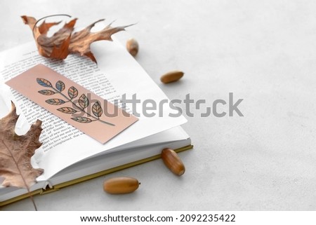 Book with bookmark, dry autumn leaves and acorns on light background