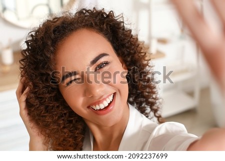 Young African-American woman with healthy hair taking selfie in bathroom, closeup