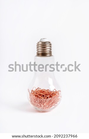 A light bulb filled with copper paper clips on a white background. Stationery objects