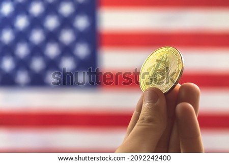 Hand with bitcoin and USA flag on background. Cryptocurrency and United States of America concept  Royalty-Free Stock Photo #2092242400