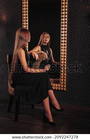 Portrait of pretty cute teenager girl in an elegant dress at mirror in dark stylish interior of living room. Children emotions and posing. Concept of style, fashion and beauty. Copy space for site