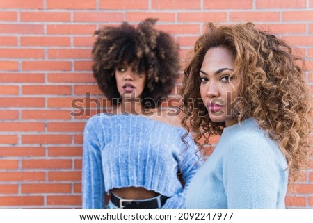 Attractive African American women with long afro hair, glamour makeup and blue shirt posing in brick wall. Beauty portrait of natural girls in brick wall. 
