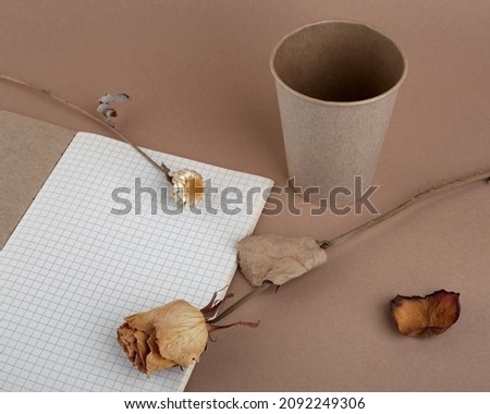 Blank notepad on a brown background. A dried flowers are on the notebook. Disposable paper cup beside the pad. Free space for your brand