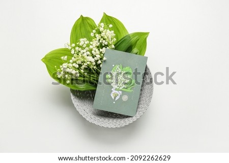 Basket with beautiful lily-of-the-valley flowers and greeting card on light background