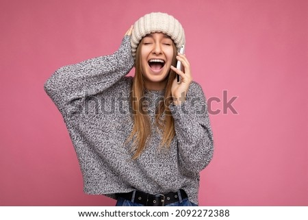 Closeup photo of Beautiful attractive positive happy amazing funny joyful young blonde woman wearing casual grey sweater and beige hat isolated over pink background with copy space holding in hand
