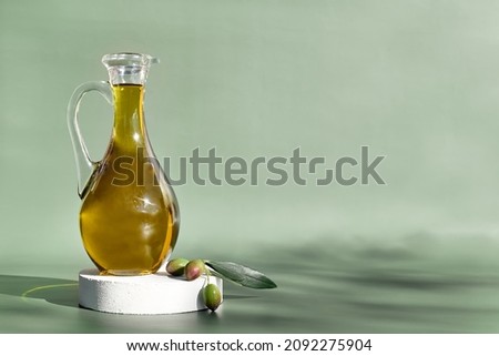 Extra virgin olive oil and olive branch in the bottle on white podium on light green background. Healthy mediterranean food. Royalty-Free Stock Photo #2092275904