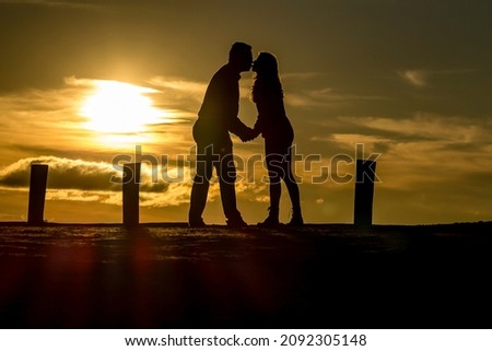 Silhouette of a couple on a mountain with a beautiful sunset on the horizon with some clouds