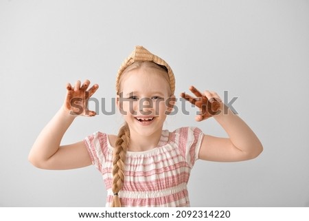 Cute little girl with chocolate on hands and face against light background