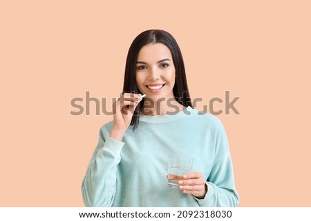 Beautiful young woman taking pills on color background Royalty-Free Stock Photo #2092318030