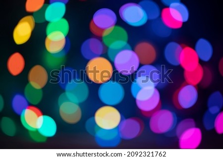 Defocused Christmas lights of blue, red, yellow and green with shades of very peri from a multicolored garland hugging the sphere