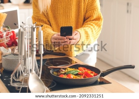 Female food photographer with mobile phone taking picture of tasty fried vegetables in kitchen