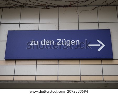 A blue sign on a tile wall showing the way to the trains. In German language it is written "to the trains“.
