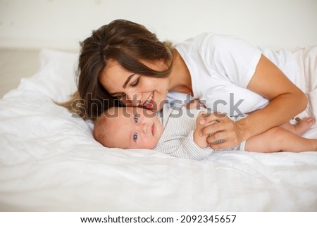 happy mom kisses baby lying on the bed in the bedroom. mom and baby are lying at home on the bed. Happy young mom hugs her little daughter in bed.  