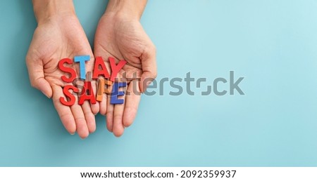 Hands showing multicolor wooden alphabet words "stay safe" on blue background. Stay Safe Message on Palm of Hand. Royalty-Free Stock Photo #2092359937