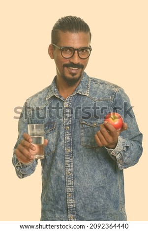 Studio shot of young bearded Indian man with denim shirt isolated against white background