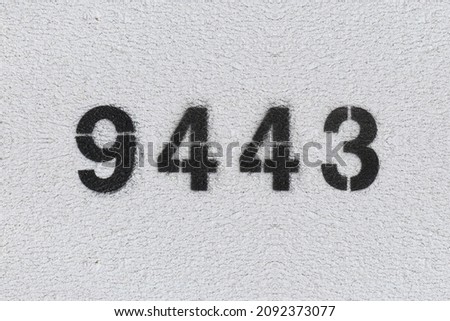 Black Number 9443 on the white wall. Spray paint. Number nine thousand four hundred and forty three.