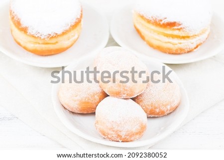 Donuts with powdered sugar and cream in saucers with a kitchen napkin lie on a white wooden table, close-up side view. Hanukkah celebration concept.