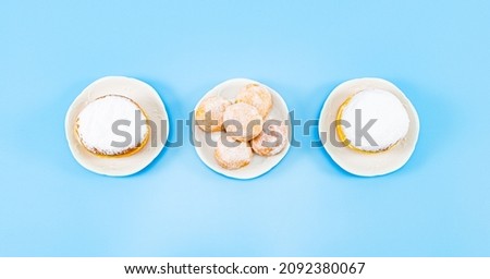 Large and small donuts with powder and cream in saucers lie in the center on a blue background, close-up flat lay. Hanukkah Celebration Concept.