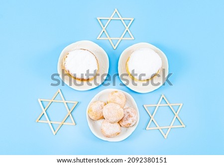 Large and small donuts with powder and cream in three saucers and three do-it-yourself wooden daid stars lie in the center on a blue background, flat lay close-up. Hanukkah Celebration Concept.