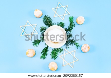 Donut with powdered sugar in a saucer on fir branches, three wooden stars of David and small donuts around lie on a blue background, top view close-up. Hanukkah celebration concept.