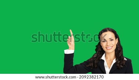 Young happy smiling woman in black confident suit, showing pointing at copy space. Business concept. Green colour background. Brunette businesswoman. Empty area for text. Chroma key back