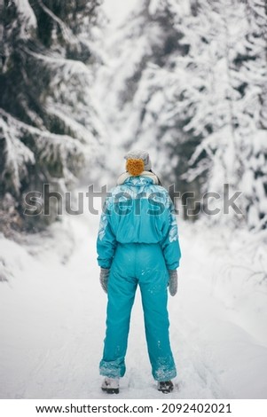 Young woman winter in full height outdoors. Unrecognizable young adult girl in ski suit standing in the mountain snowy forest, back view