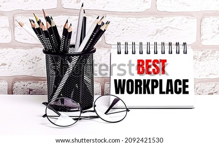 A workplace in the house with glasses, pencils in a stand and a notebook with text BEST WORKPLACE on a brick wall background. Home office. Scandinavian style