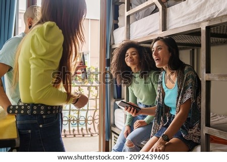 Women students talking about a social network content on the smartphone screen sitting on bunk bed of an hostel room Royalty-Free Stock Photo #2092439605