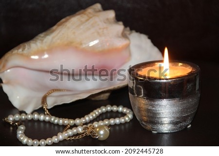 A large white seashell, pearls and a candle on a dark background