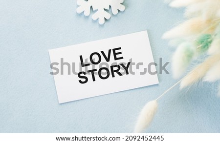 Love Story inscription on a card that lends on a blue background next to fluffy branches of dried flower, festive background