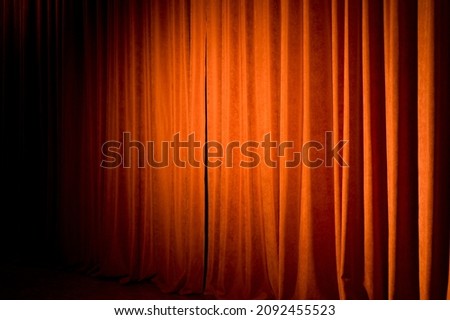 A red-orange theater curtain illuminated by spotlights in a semi-dark theater hall.