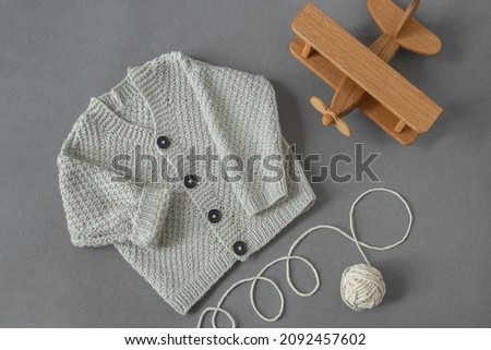 knitted children's cardigan with a ball of natural yarn on a gray background with a wooden toy in retro style, baby  layout Royalty-Free Stock Photo #2092457602