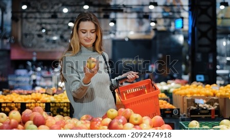 Young business woman girl buyer client blonde lady consumer stands in shop near counter with fruits in grocery store supermarket choosing juicy ripe apples for juice diet food buying puts in basket Royalty-Free Stock Photo #2092474918