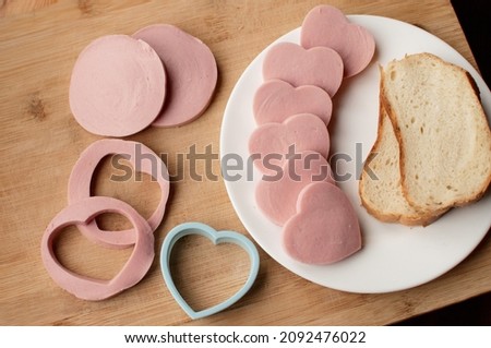 white bread and boiled sausage for making sausage sandwiches in the form of hearts on a wooden background with a plastic mold for cutting Royalty-Free Stock Photo #2092476022