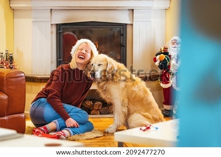 Young woman celebrating New Year at home with her dog. Dog is wearing costume, she is smiling and enjoy in holiday. Photo of young woman and her dog enjoying together at home in a Christmas atmosphere