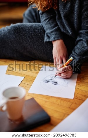 Close up of an artistic girl sitting on the floor in the morning and drawing portraits. She is enjoying her morning moments with a cup of fresh coffee.