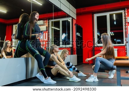 Four tired, happy athletic girls chat and relax after a hard workout in the gym