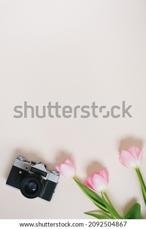 Minimal feminine home desktop with pink tulip and old camera on beige background. Flat lay, top view. Spring concept