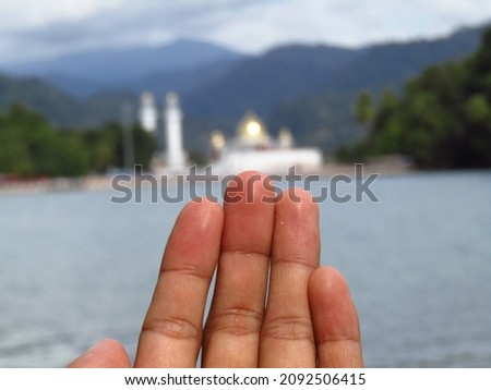 photo of left hand finger with sea and mosque background