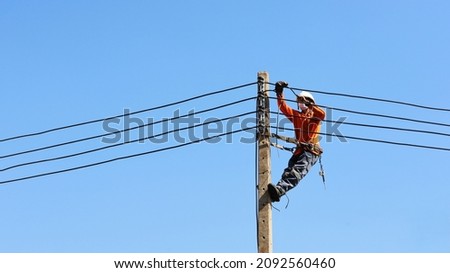 Technician connecting wires on electric poles. Employees hung with belts on electric poles to install low voltage cables on concrete poles on a blue sky background with copy space. selective focus Royalty-Free Stock Photo #2092560460